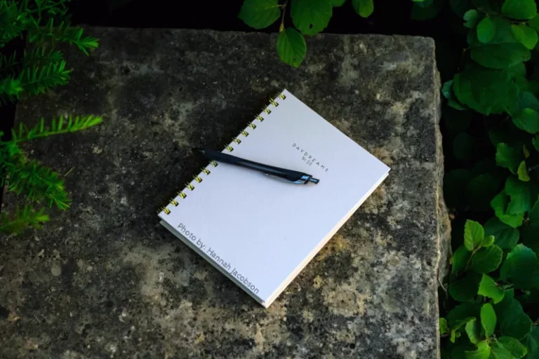 A journal outside on top of a marble block with plants around it. beginner shadow work prompts.