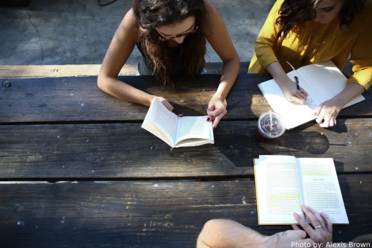 Bird's eye view of three students with open books studying at an outdoor table. How to manifest good grades.