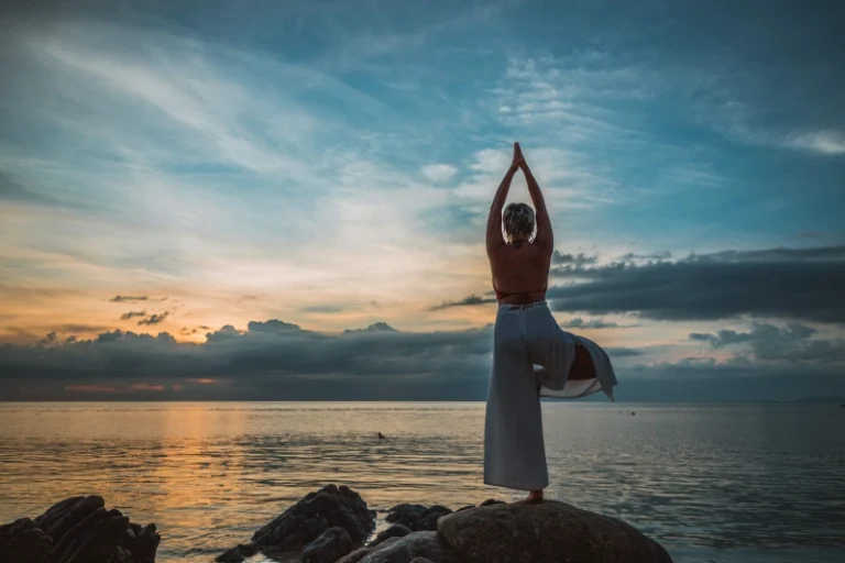 Woman standing on one leg on a large rock overlooking a lake doing a yoga Pose. Manifest weight loss