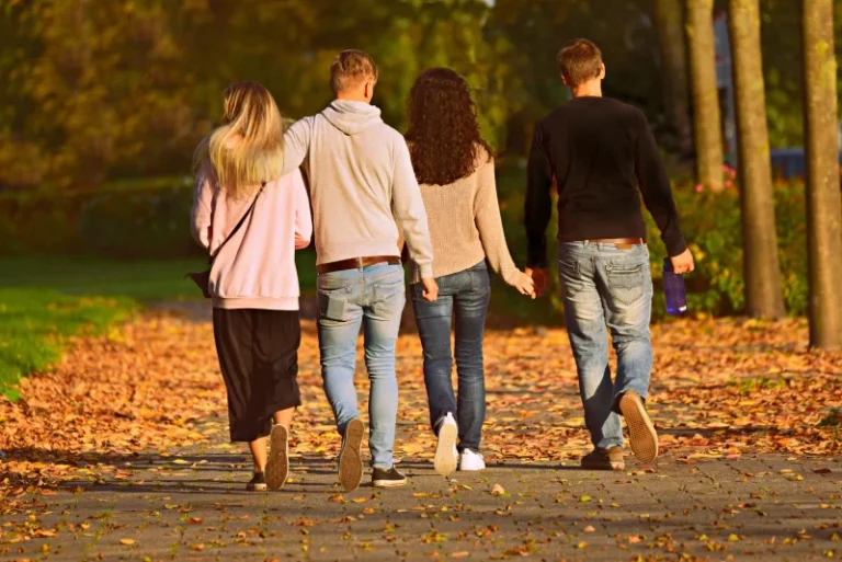 Back view of a group of friends walking through a park in Autumn. How to manifest friends.