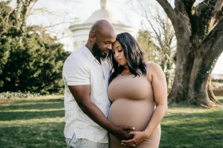 A couple standing outside, with the husband’s hand on his wife's pregnant stomach. How to manifest pregnancy.