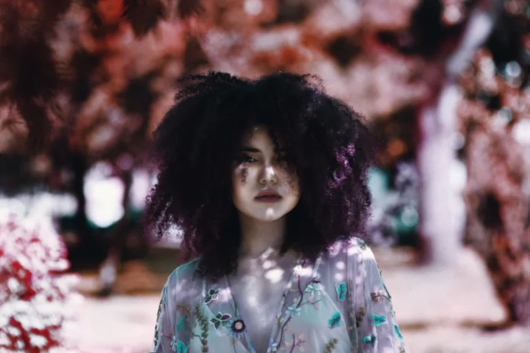 A woman with purple curly hair walking through a park, symbolizing how to manifest curly hair.