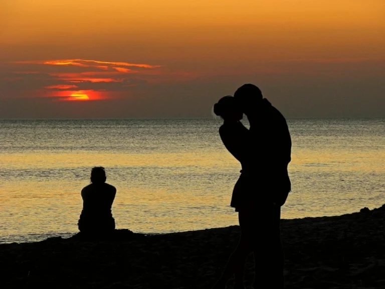 Silhouette of a person sitting alone by a lake during a sunset. Next to this person is a vision they are having of them and their ex back togther in eachothers arms. How to manifest your ex back.