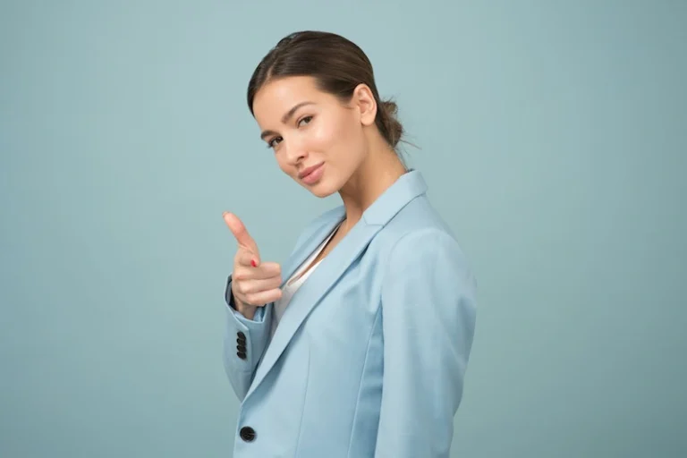 Confident woman wearing a light blue suit pointing at you. Become more confident and assertive.