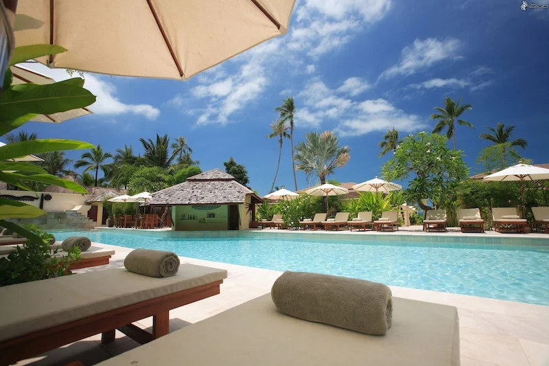 Tranquil poolside retreat with lounge chairs under colorful umbrellas, towels neatly folded, beside a clear blue pool. Manifesting a dream vacation.