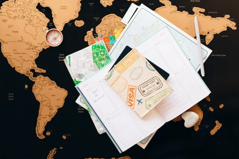 A travel visa and documents spread out on a table, atop a black and orange world map. How to manifest a visa.