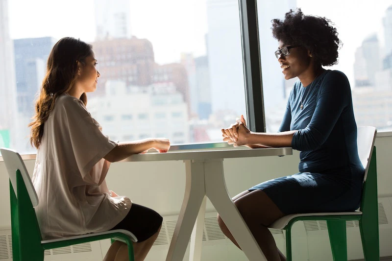 Two people sitting at a table across from each other having a conversation. How to manifest communication.