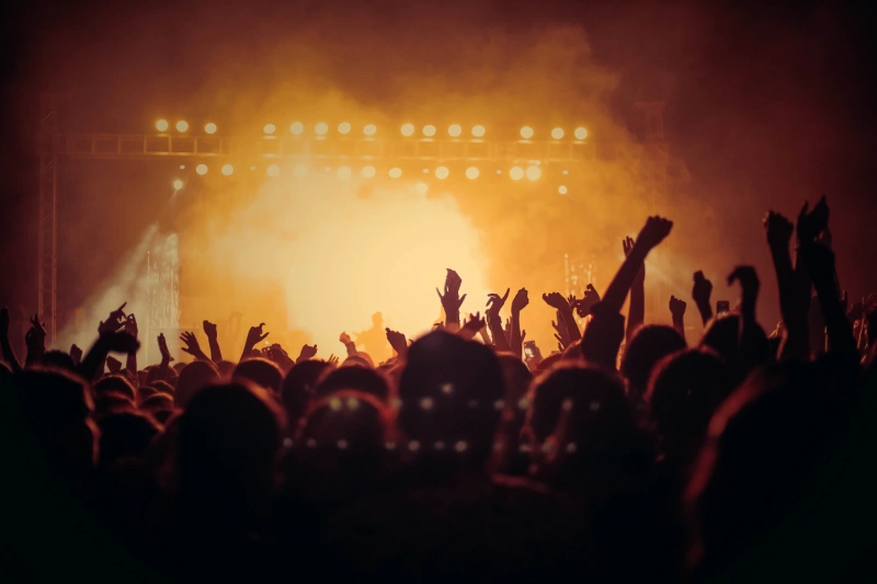 A crowd of people with their hands up in the air, dancing near a stage. How to manifest concert tickets.