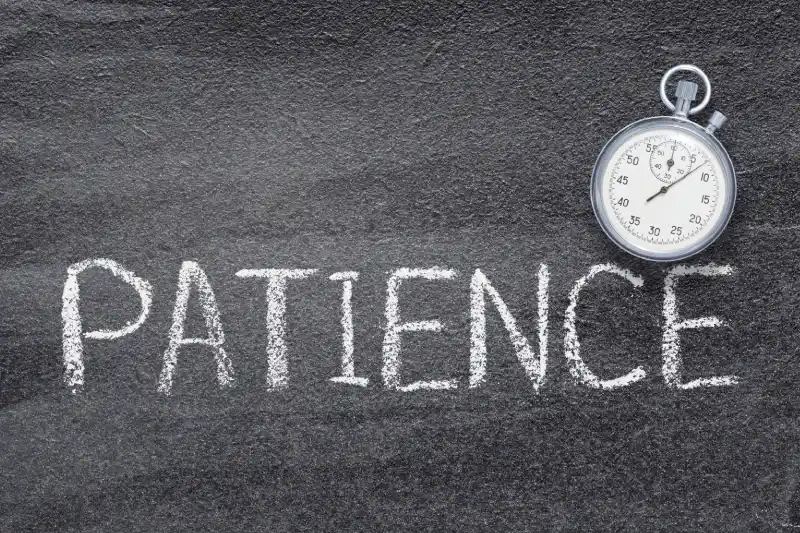 Image of the word "Patience" written in chalk on the ground with a stopwatch next to it.