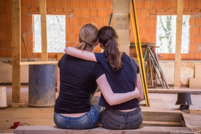 Two friends sitting back to camera, each with one arm around the other, embodying manifesting bestie goals.